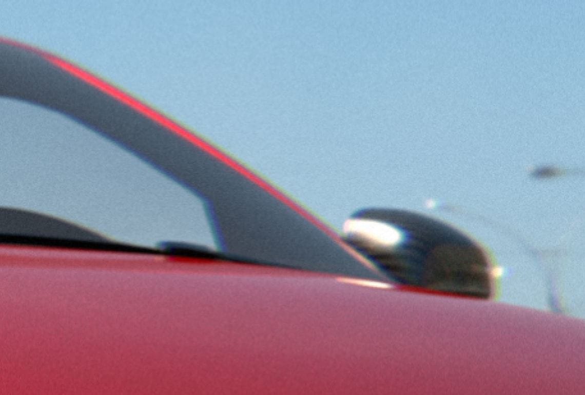 a red car's wing mirror with chromatic aberration